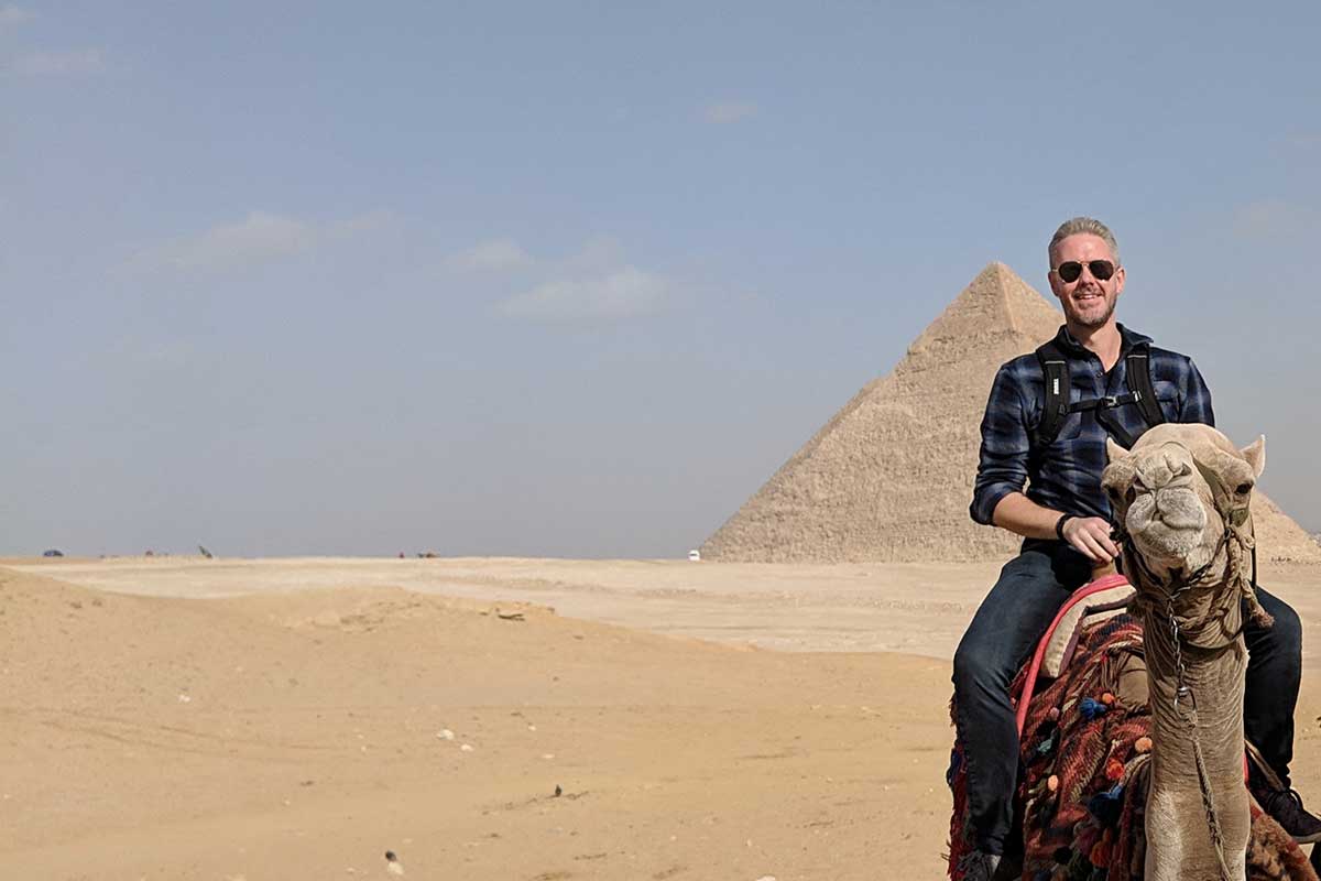 Bret McGowen sitting on a camel in front of an Egyptian Pyramid
